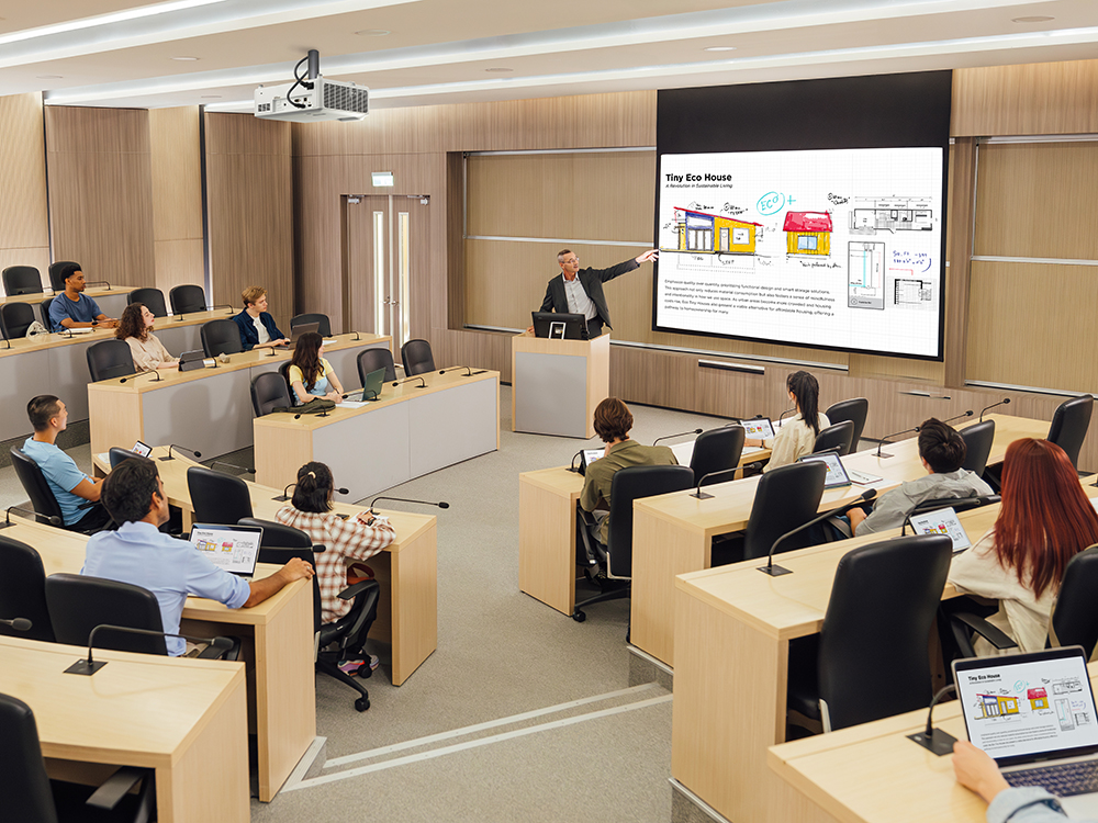 Professor delivering a lecture using large-format projector in a packed university auditorium